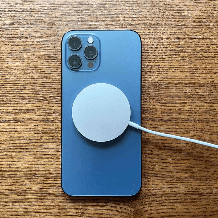 Ahşap yüzeyde mavi iPhone'un arkasına manyetik olarak hizalanmış MagSafe kablosuz şarj aleti